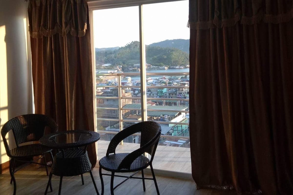 Ein Zimmer mit großem Fenster, zwei Korbstühlen und einem kleinen Tisch.