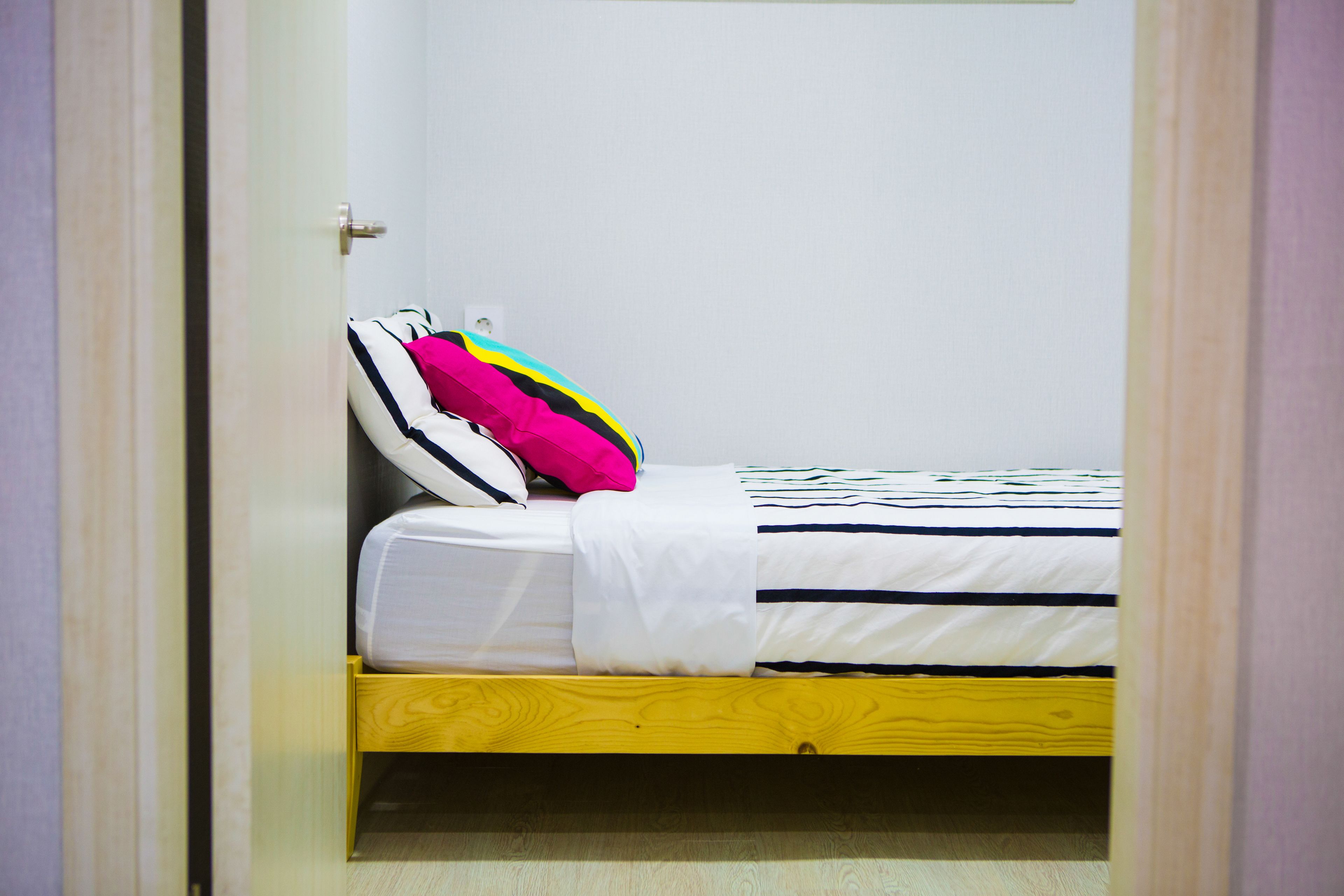 A single bed with a white and black striped bedspread, a white blanket, and a wooden headboard.