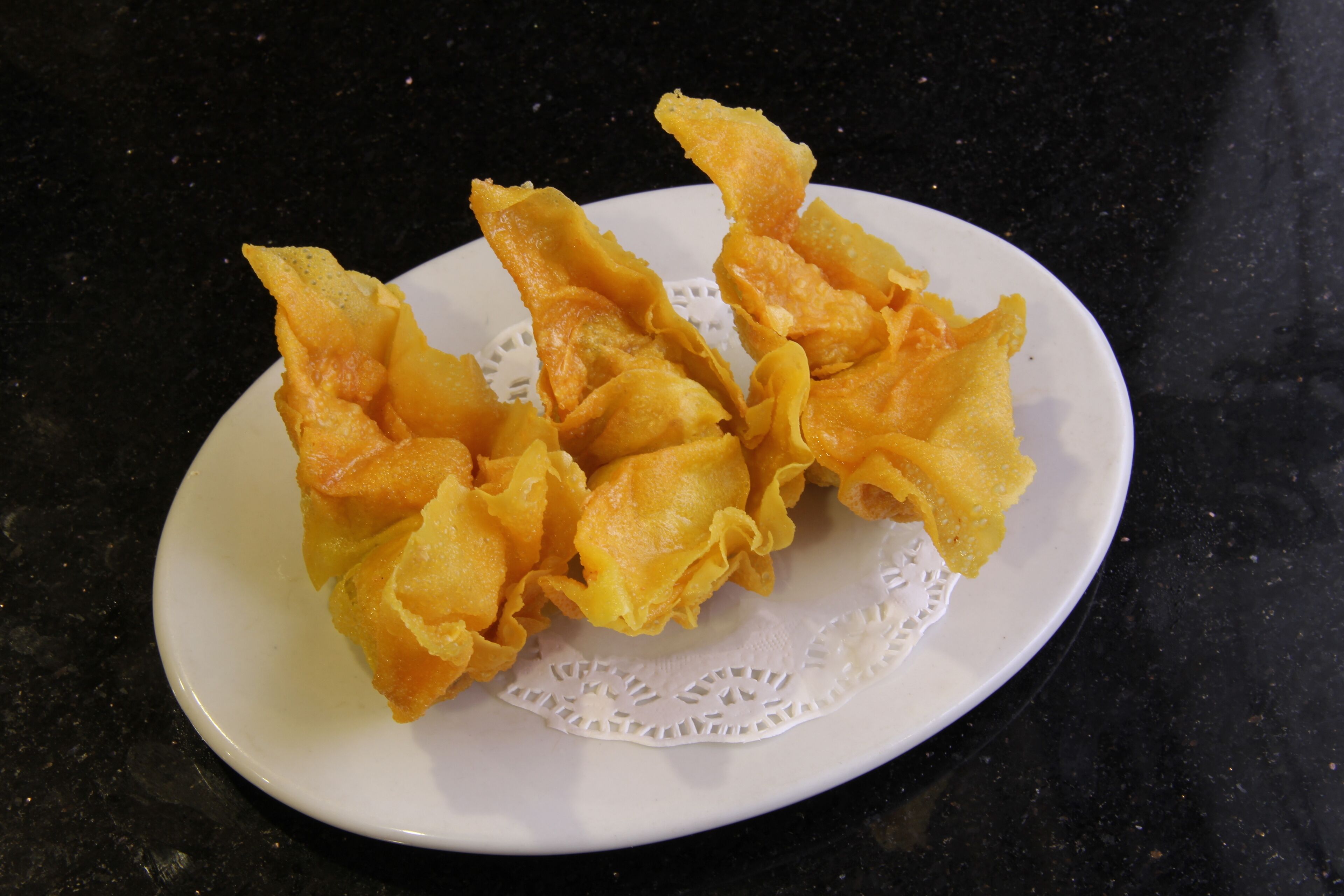 A white plate with golden-brown fried items on a black countertop.