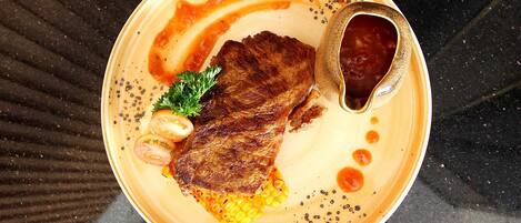 A plate with a steak, corn, and a sauce.