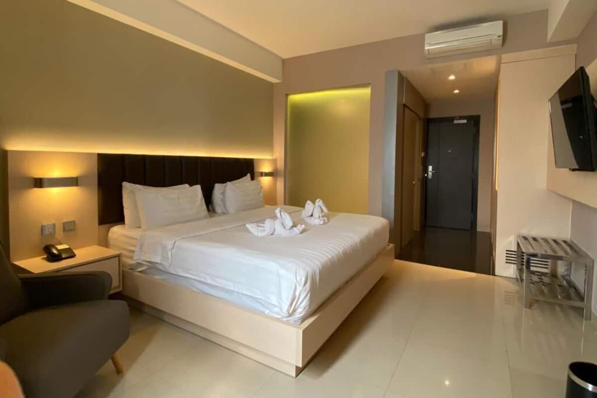 A modern hotel room with a large bed, bedside tables, a TV, and an air conditioning unit.