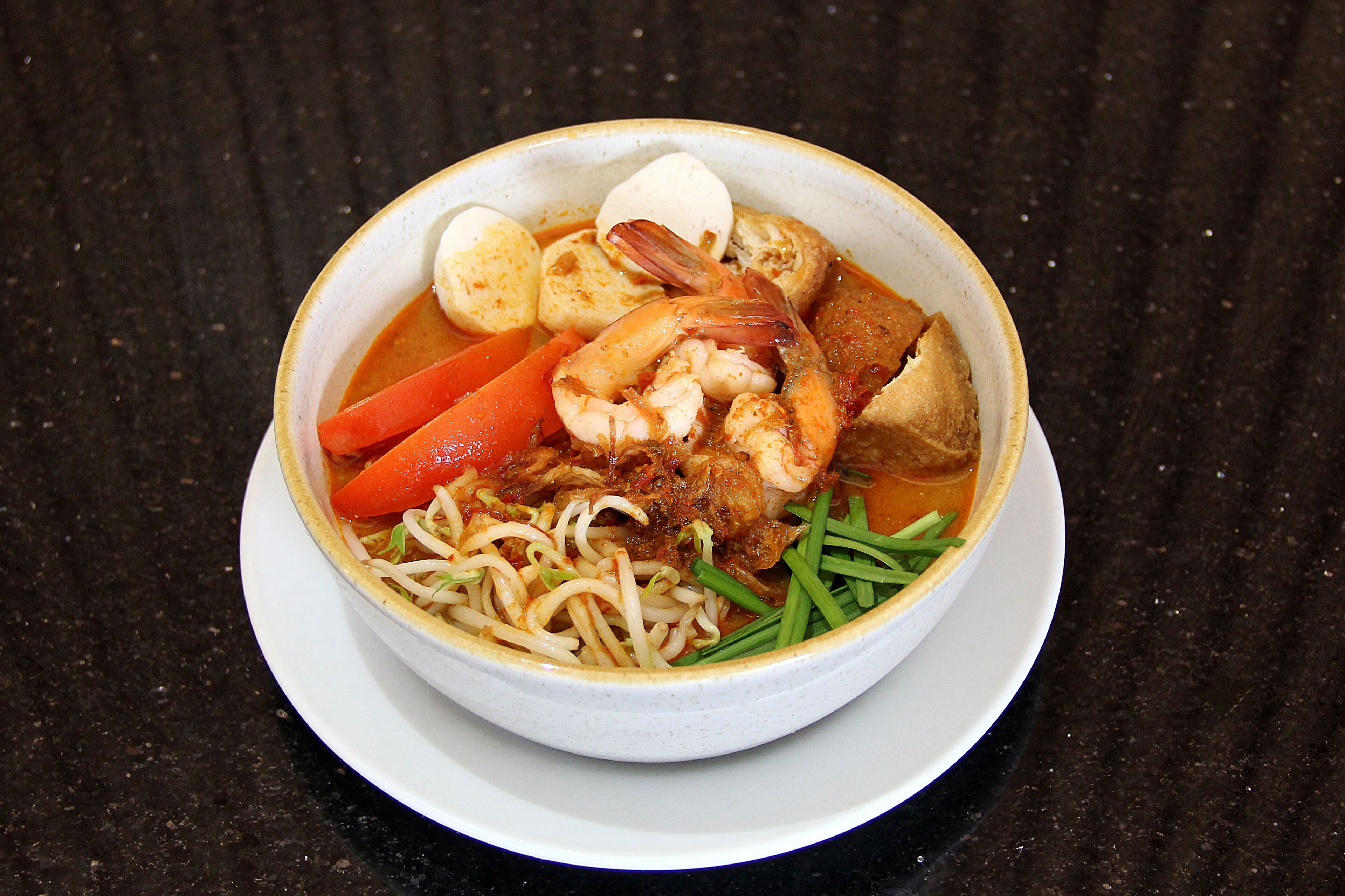 A bowl of noodle soup with shrimp, eggs, and vegetables.