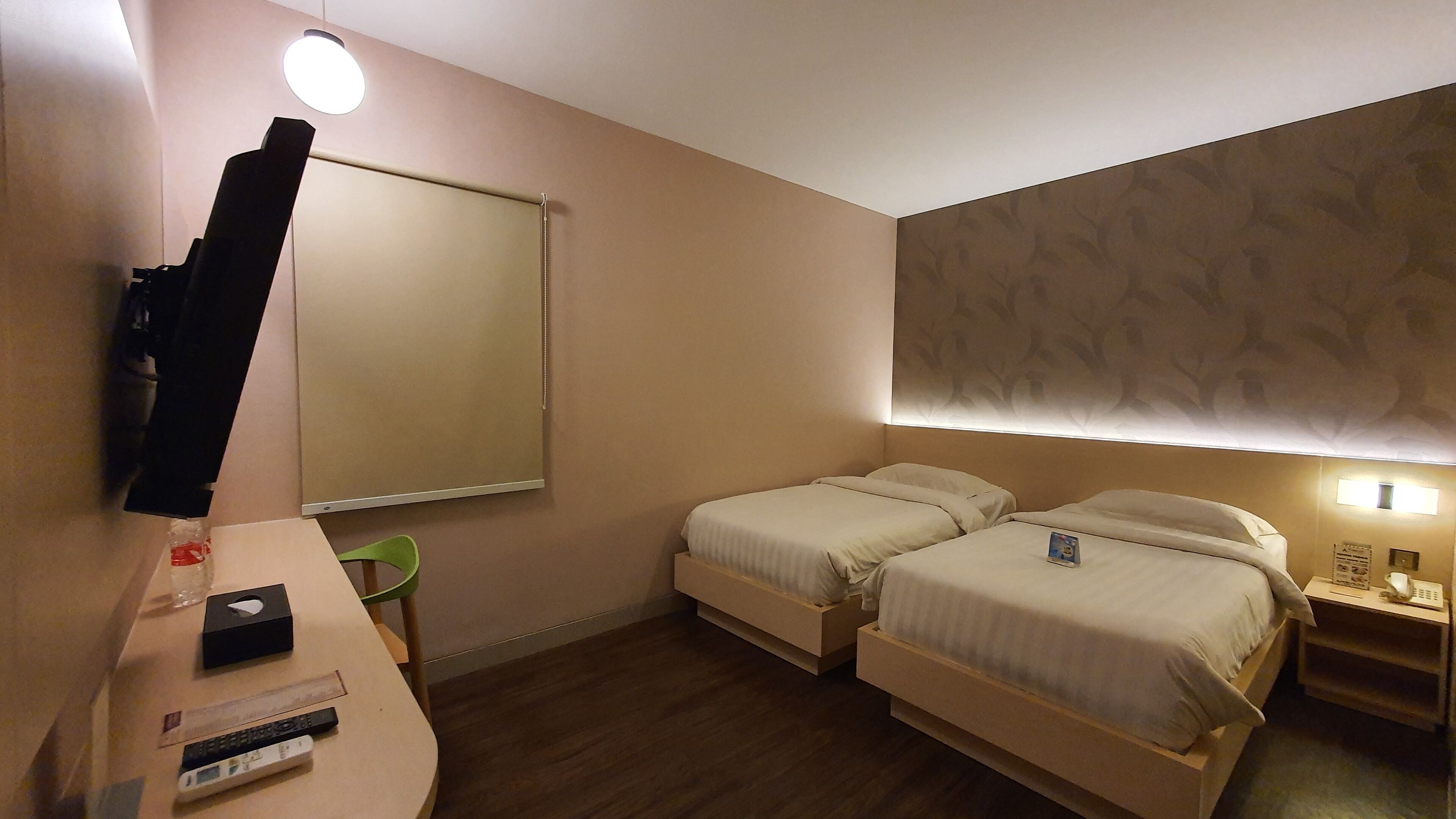 A hotel room with two single beds, a desk with a lamp, a chair, and a large mirror.