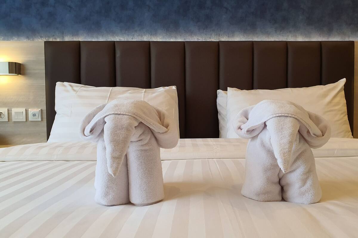 A hotel room with a large bed, two towels shaped like elephants, a dark headboard, and wall-mounted lights.