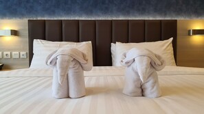 A hotel room with a large bed, two towels shaped like elephants, a dark headboard, and wall-mounted lights. - Classie Hotel (Palembang)
