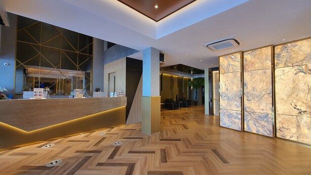 Un moderno vestíbulo de hotel con suelo de madera en patrón de espiga, una recepción con diseño geométrico en la pared y una gran pared de mármol.