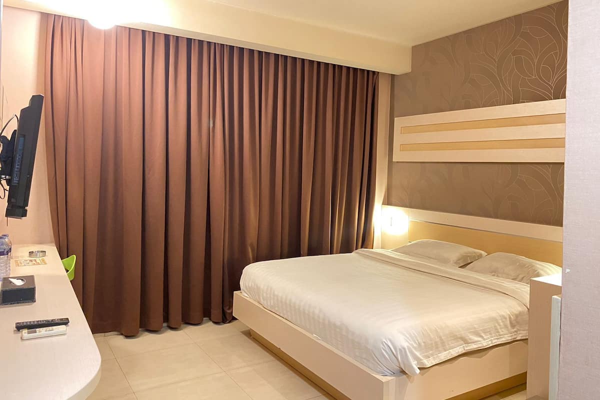 A hotel room with a bed, a bedside table, a mirror, and a curtain.
