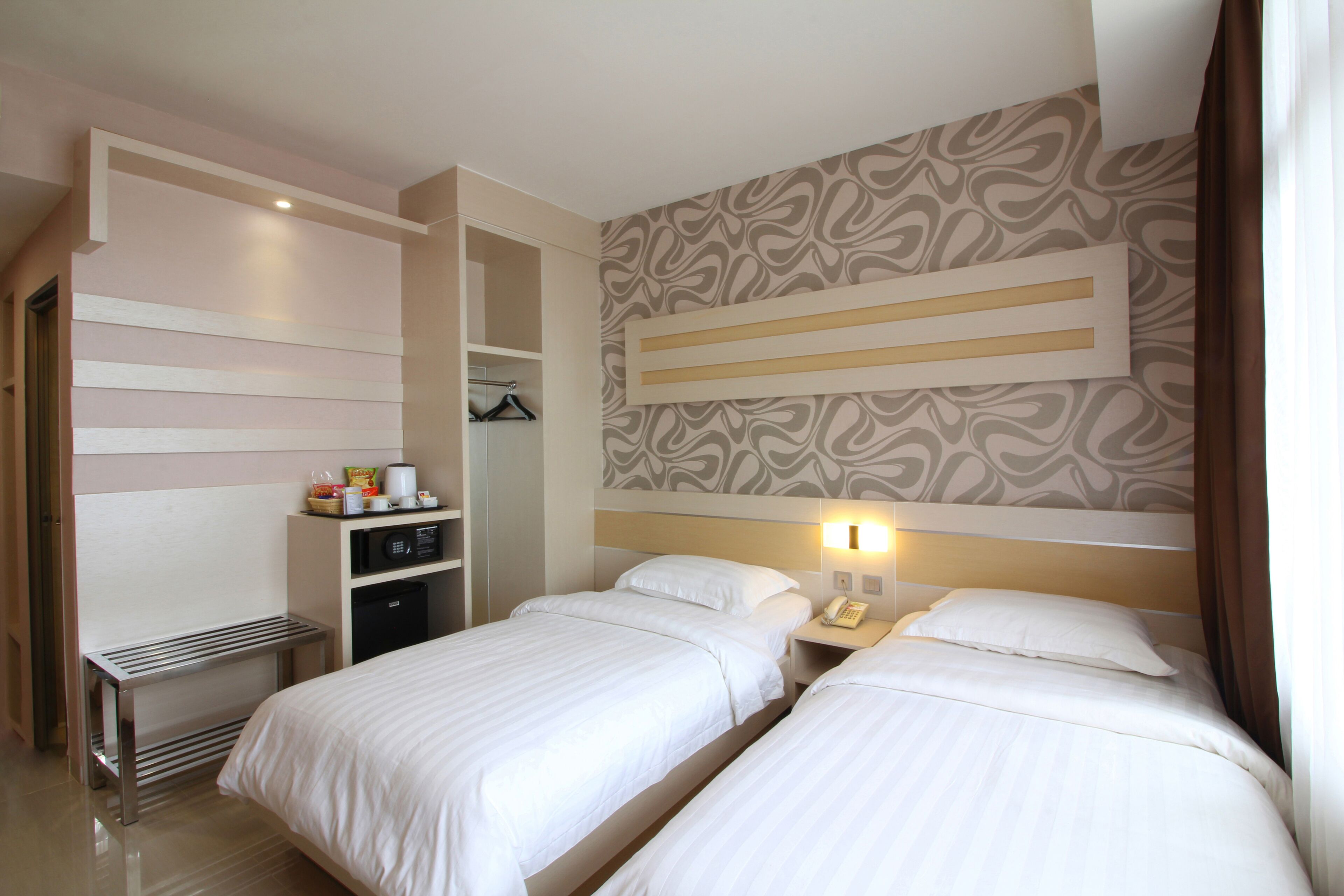 Habitación de hotel con dos camas, un escritorio, un armario y un papel tapiz estampado.