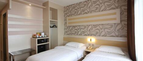 Habitación de hotel con dos camas, un escritorio, un armario y un papel tapiz estampado.