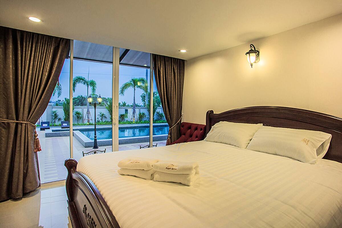 A hotel room with a large bed, a view of a swimming pool, and a balcony.