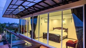 A modern bedroom with a glass wall, a bed, and a small seating area. - Royal Graces Pool Villas (Cha-am)