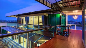 A modern hotel with a glass balcony, a rooftop terrace, and a view of the city skyline. - Royal Graces Pool Villas (Cha-am)