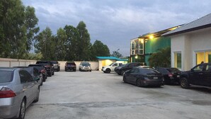 A parking lot with several cars, a building with a green roof, and trees in the background. - Royal Graces Pool Villas (Cha-am)