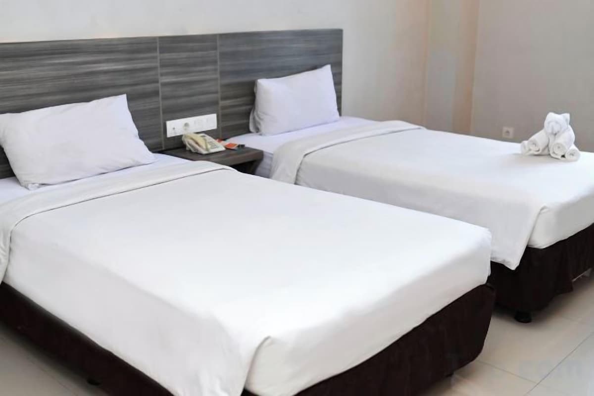 Two twin beds with white linens, a wooden headboard, and a bedside table with a phone.