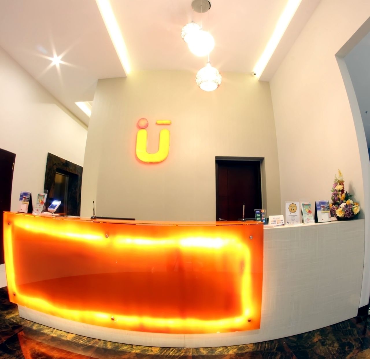 A reception desk with a U-shaped logo, a reception area, and a wall-mounted display with books and a floral arrangement.