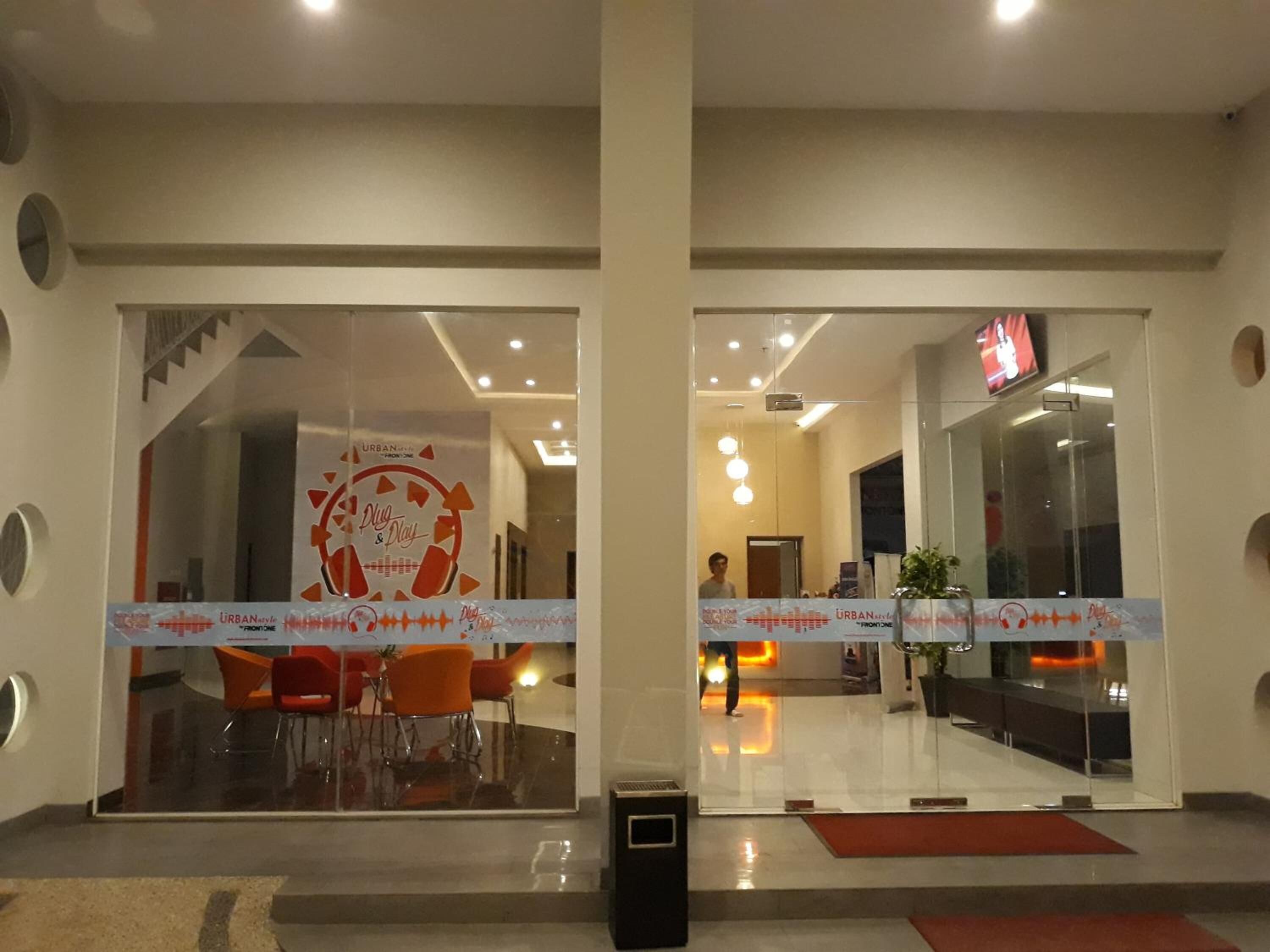 Een hotel lobby met een receptiebalie, een glazen scheiding en oranje stoelen.
