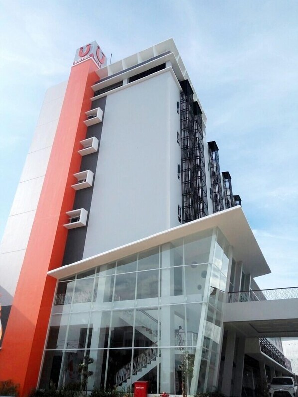 Um moderno edifício de hotel com fachada marcante em vermelho e branco, amplas janelas de vidro e uma escadaria visível que leva à entrada.