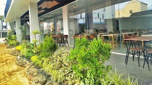 An outdoor seating area with tables and chairs, surrounded by potted plants and a stone pathway. - Urban Style Hotel Lampung, Azana Hotels Collection (Gedongtataan)
