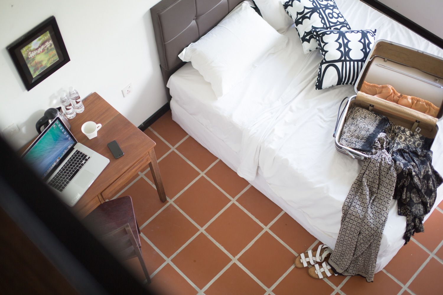 Une chambre à coucher avec un lit, une valise, un ordinateur portable, une tasse et une petite table.