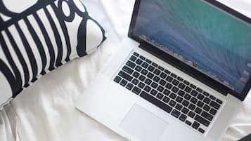 A laptop on a bed with a white and black patterned pillow.