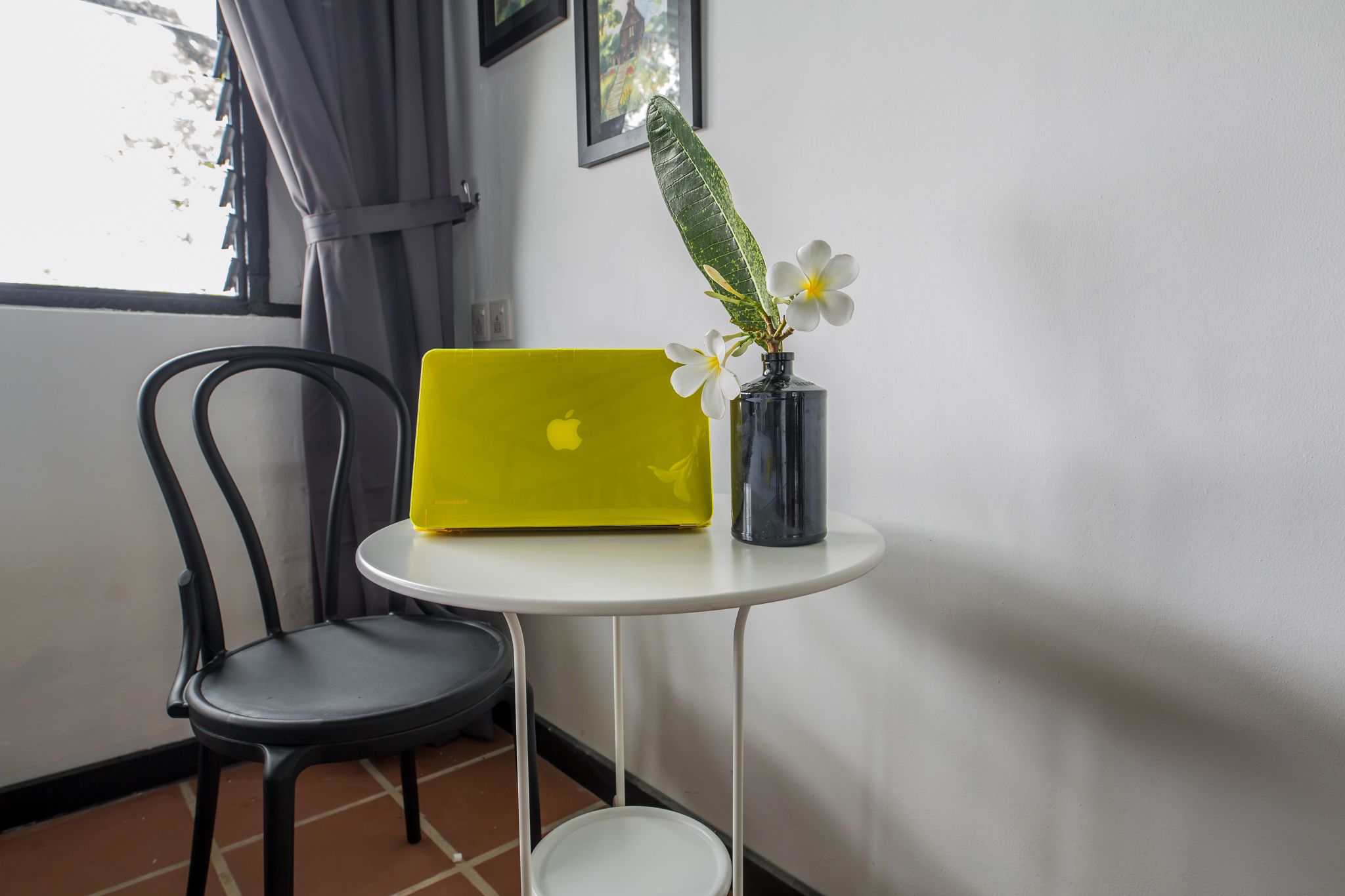 Una laptop amarilla sobre una pequeña mesa blanca, con una silla negra a su lado.