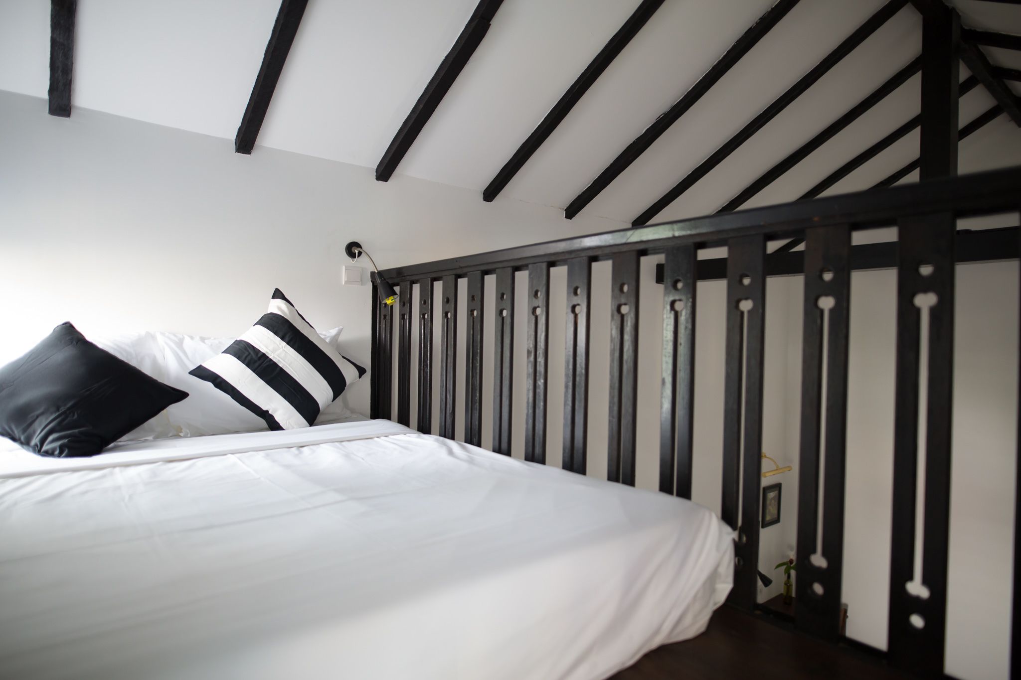 Quarto com cama, almofadas listradas em preto e branco, cabeceira de metal preto e parede branca.