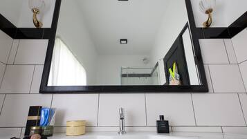 A bathroom with a large mirror, white tiles, a sink, and toiletries.