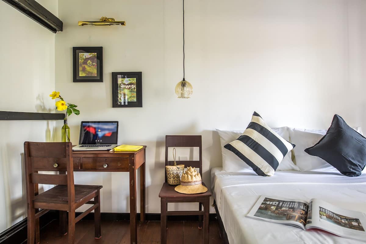 Une chambre à coucher bien rangée, avec un lit, un bureau sur lequel se trouve un ordinateur portable, une chaise et une table de chevet avec un livre.