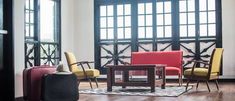 Una habitación con un sofá rojo, sillas amarillas y negras, una mesa de centro de madera y dos maletas.