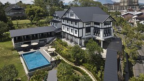 Una casa grande y moderna con piscina, rodeada de abundante vegetación y otras edificaciones residenciales.