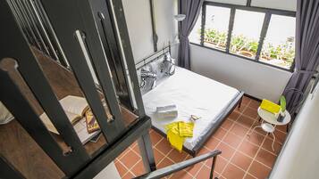 Quarto pequeno e aconchegante com uma cama, uma janela com cortinas, uma mesinha com uma planta e uma cadeira.