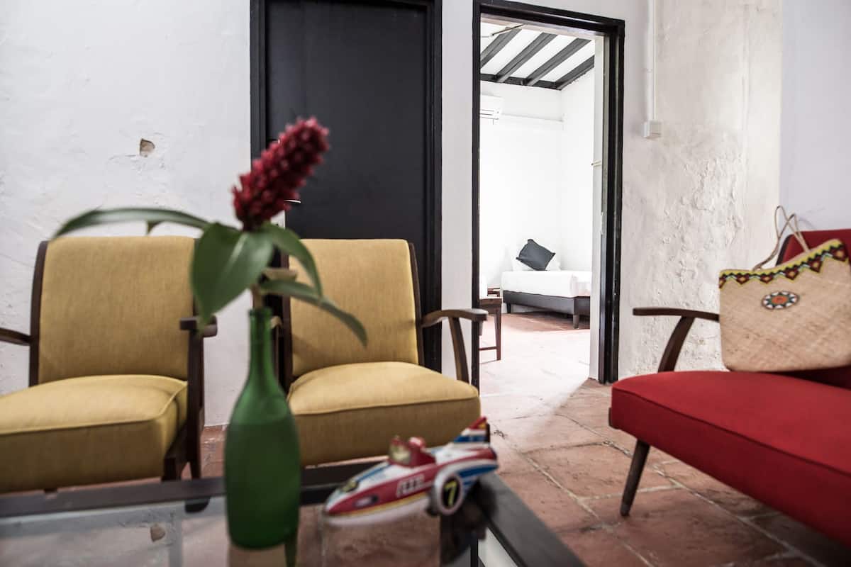 Une pièce avec deux chaises jaunes, un canapé rouge, un vase vert contenant une fleur rouge et un avion jouet posé sur une table en verre.