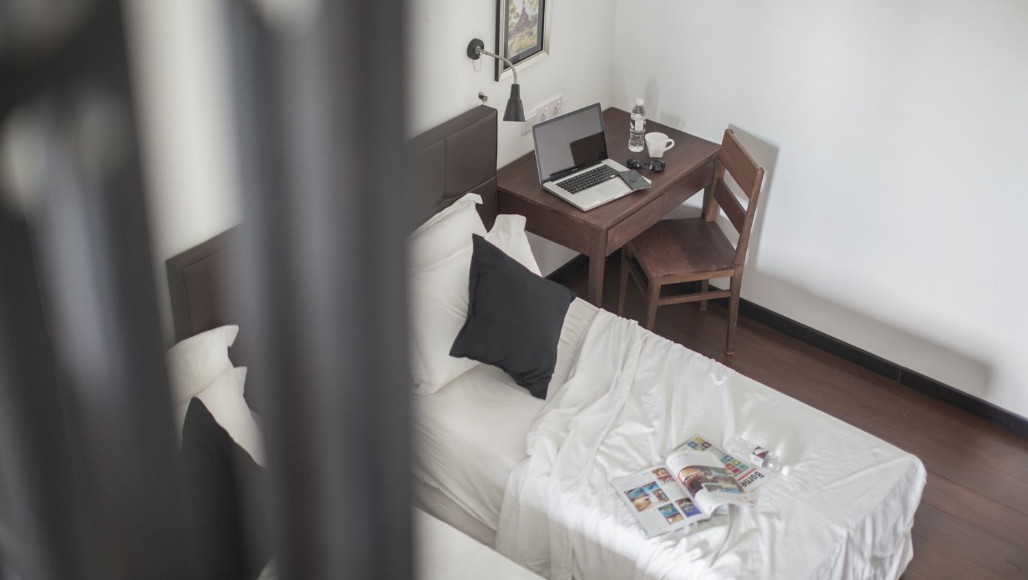 A hotel room with a bed, a desk with a laptop, a chair, and a small table with a magazine.