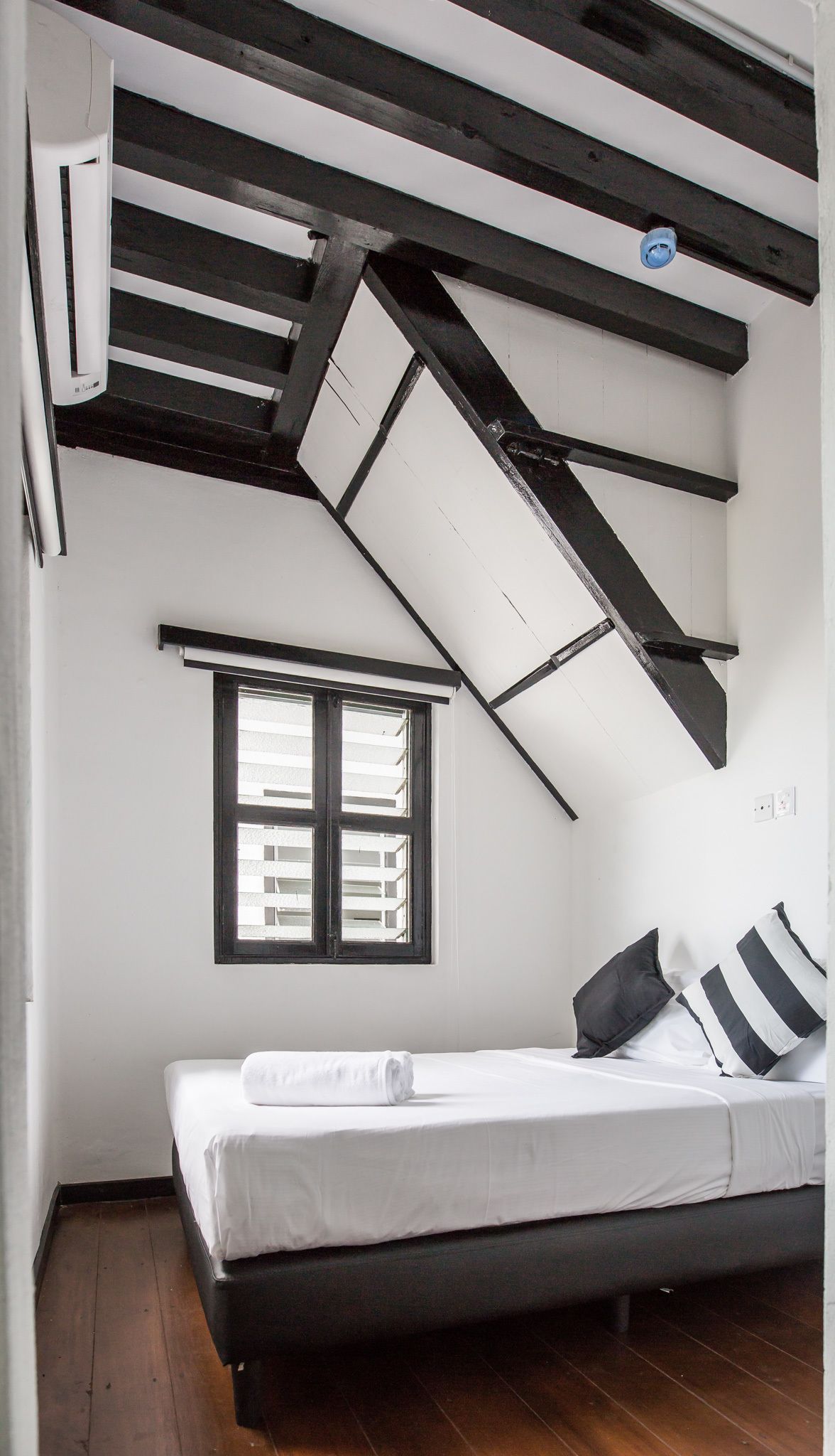 A bedroom with a sloped ceiling, a window, a bed, and a black and white striped pillow.