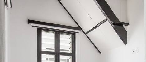 A bedroom with a sloped ceiling, a window, a bed, and a black and white striped pillow.