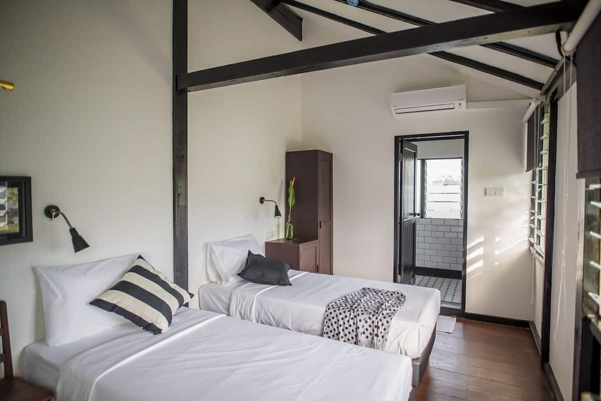 Une chambre d’hôtel avec deux lits, un plafond en bois, un appareil de climatisation, une porte donnant sur un balcon et un petit placard.