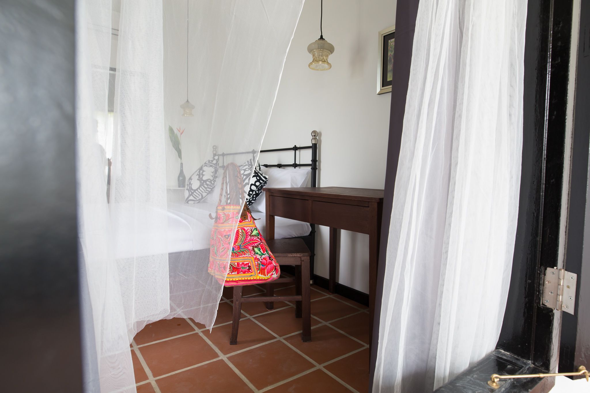 Un dormitorio con cama, una silla, una mesa y una lámpara colgante.