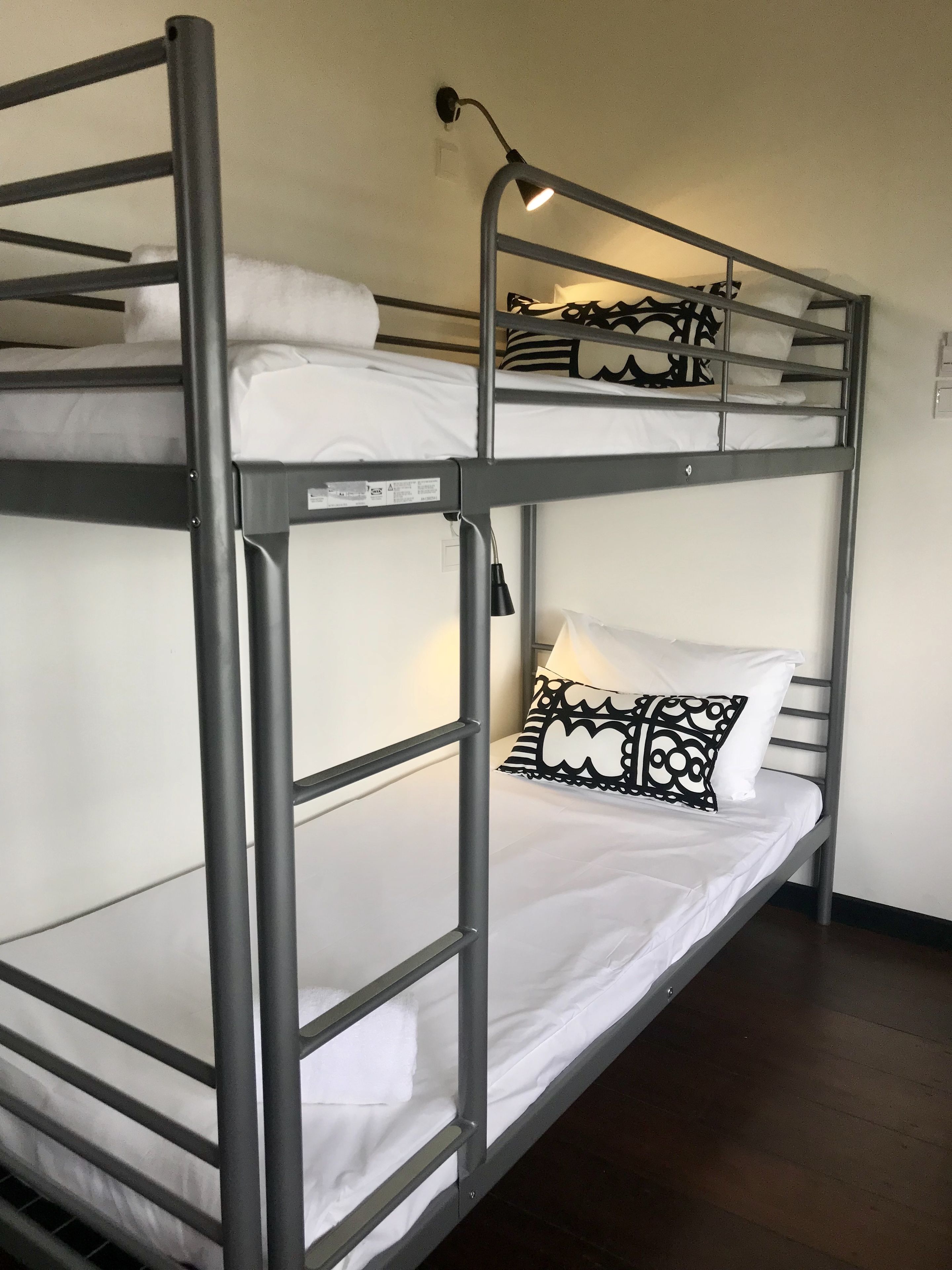 A bunk bed with a desk lamp, white bedding, and a patterned pillow.