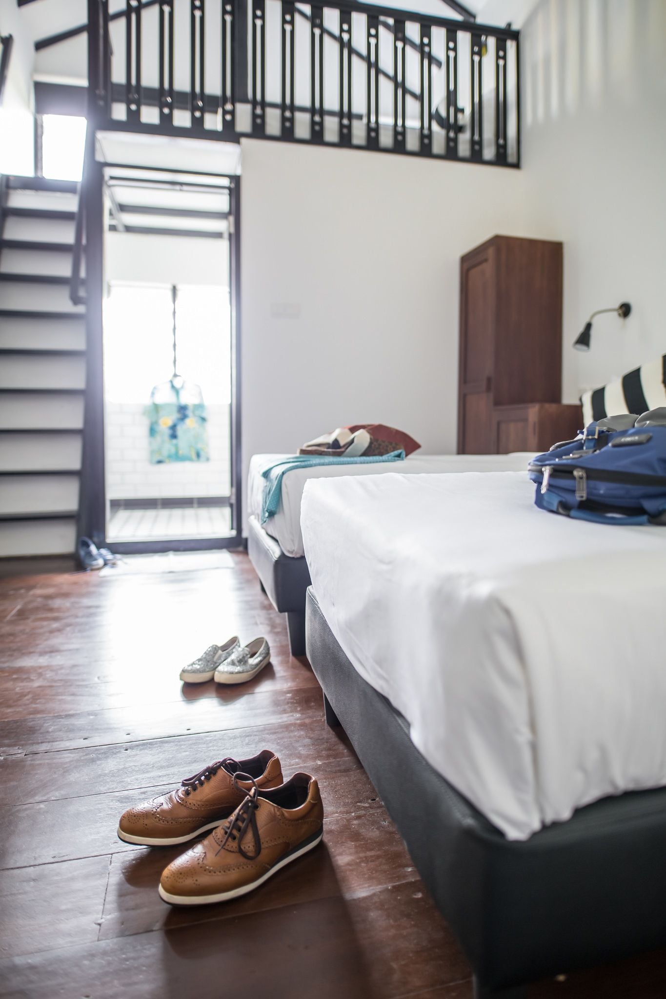 A bedroom with a bed, a wooden wardrobe, a suitcase, and a pair of shoes on the floor.