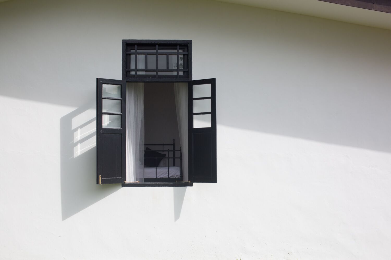A room with a single bed, a window with open shutters, and a white wall.