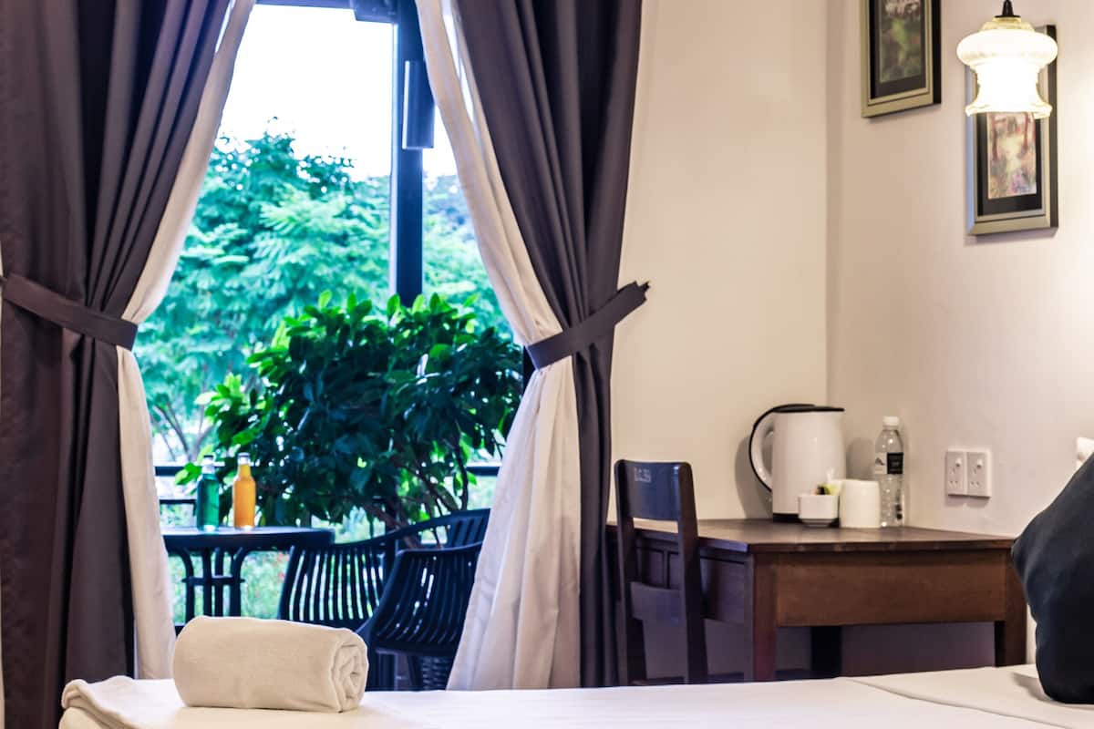 Une chambre d’hôtel avec deux lits, une table avec une bouilloire et une bouteille, et une vue sur la verdure environnante.