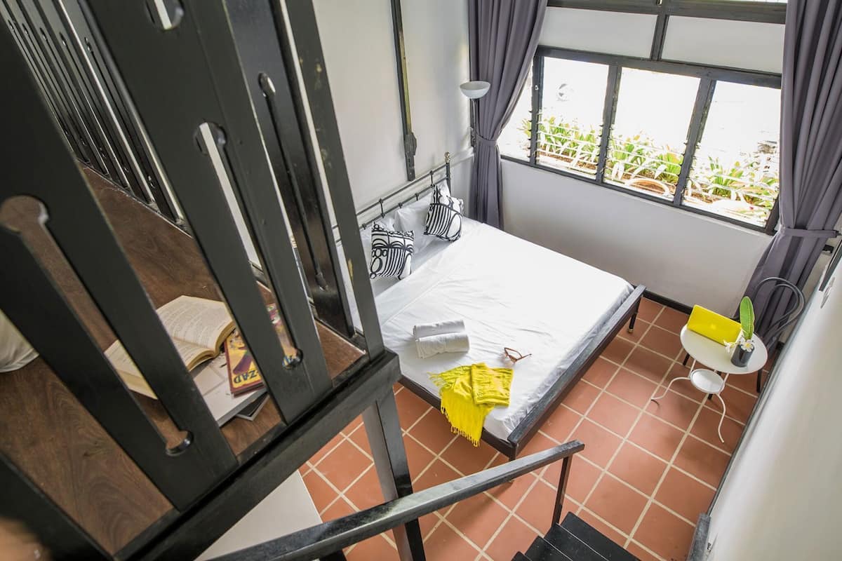 Une pièce avec un lit, une fenêtre avec des rideaux, une petite table avec une plante et une chaise.