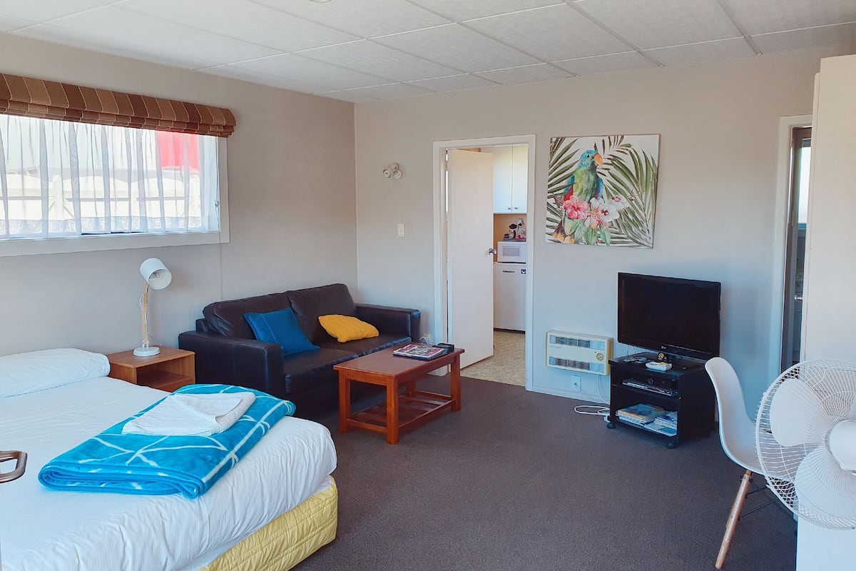 A hotel room with a bed, a sofa, a TV, a desk, and a chair.