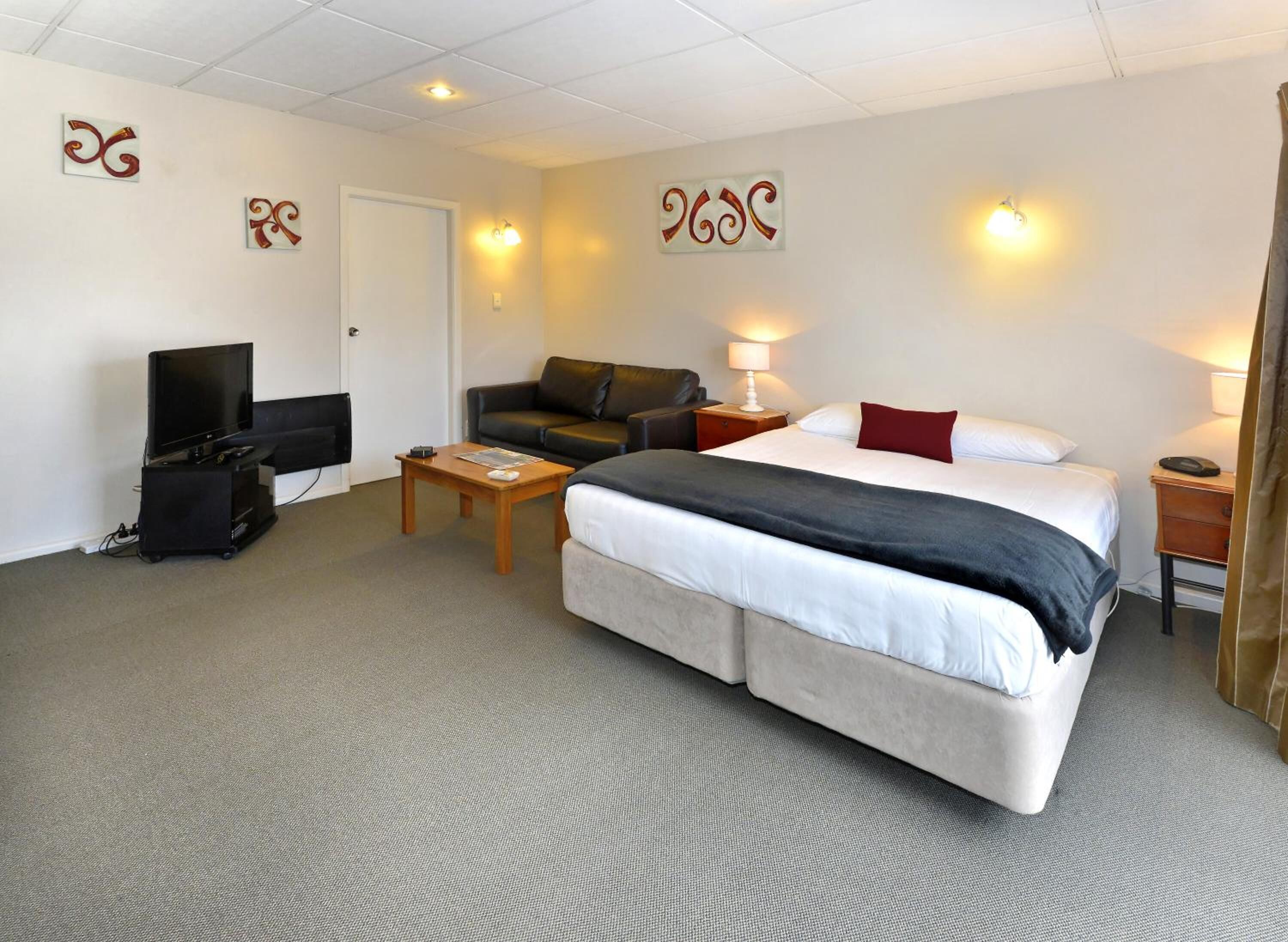 A hotel room with a large bed, a sofa, a TV, a desk, and a lamp.