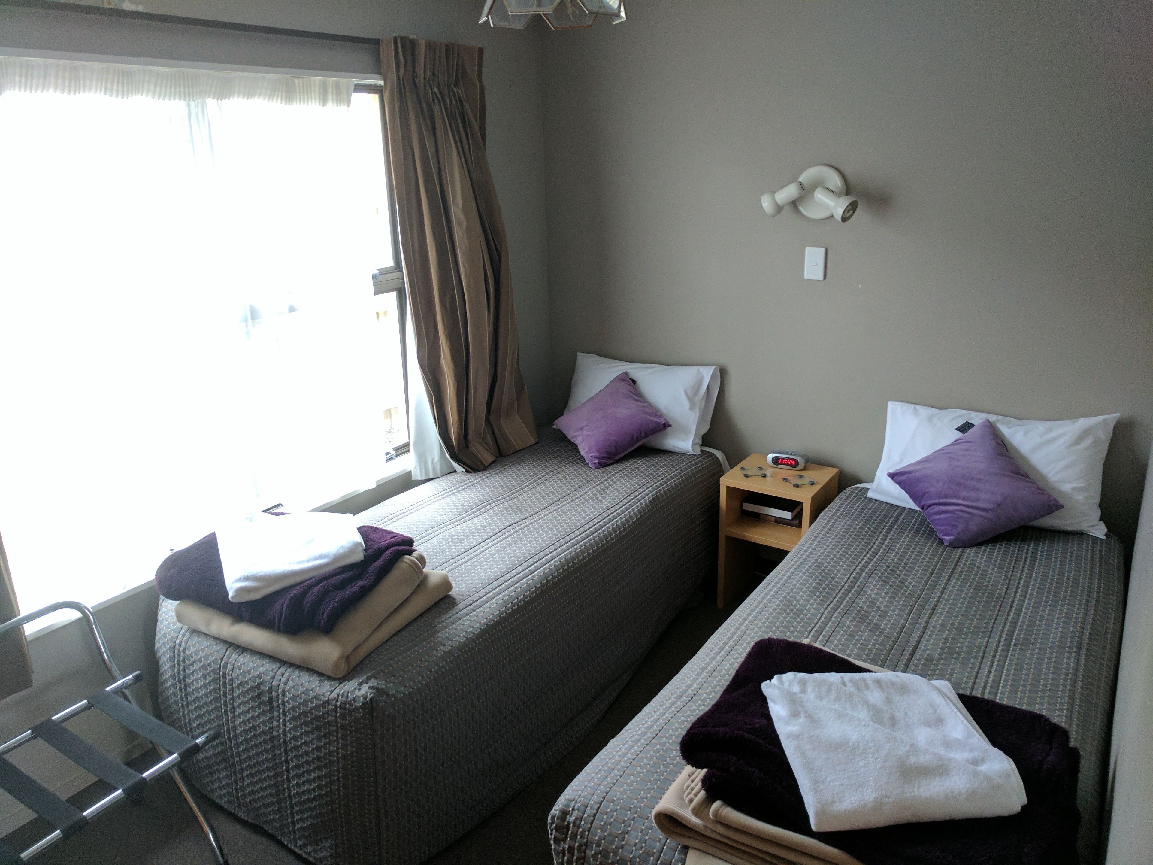 Habitación de hotel con dos camas, una mesita, una silla y un ventanal con cortinas.