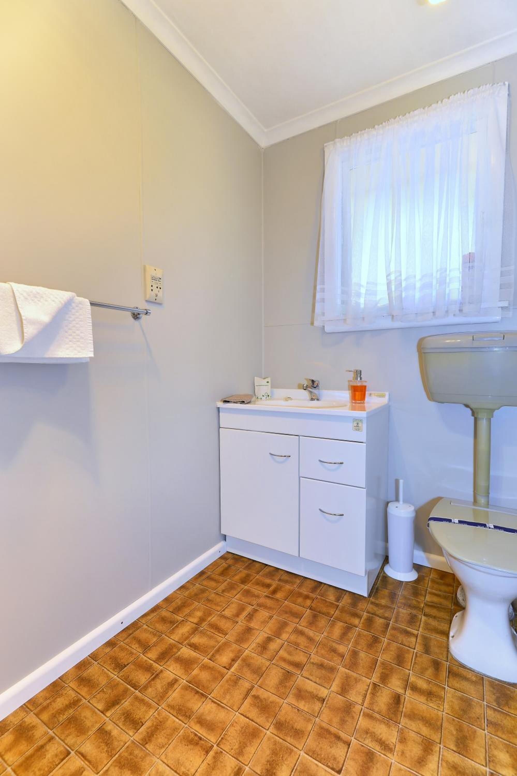A bathroom with a white sink, toilet, and a window with white curtains.