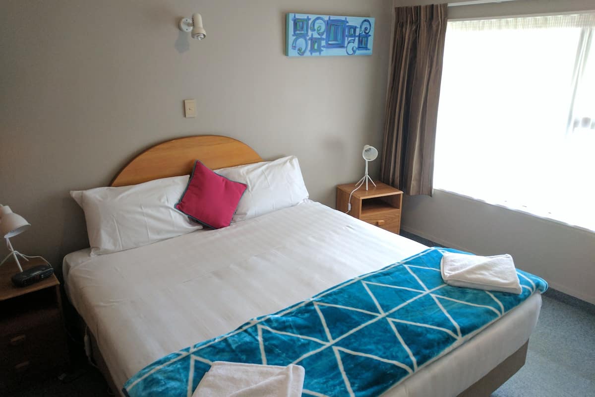 A hotel room with a bed, a nightstand, a lamp, a wall art piece, and a window with curtains.