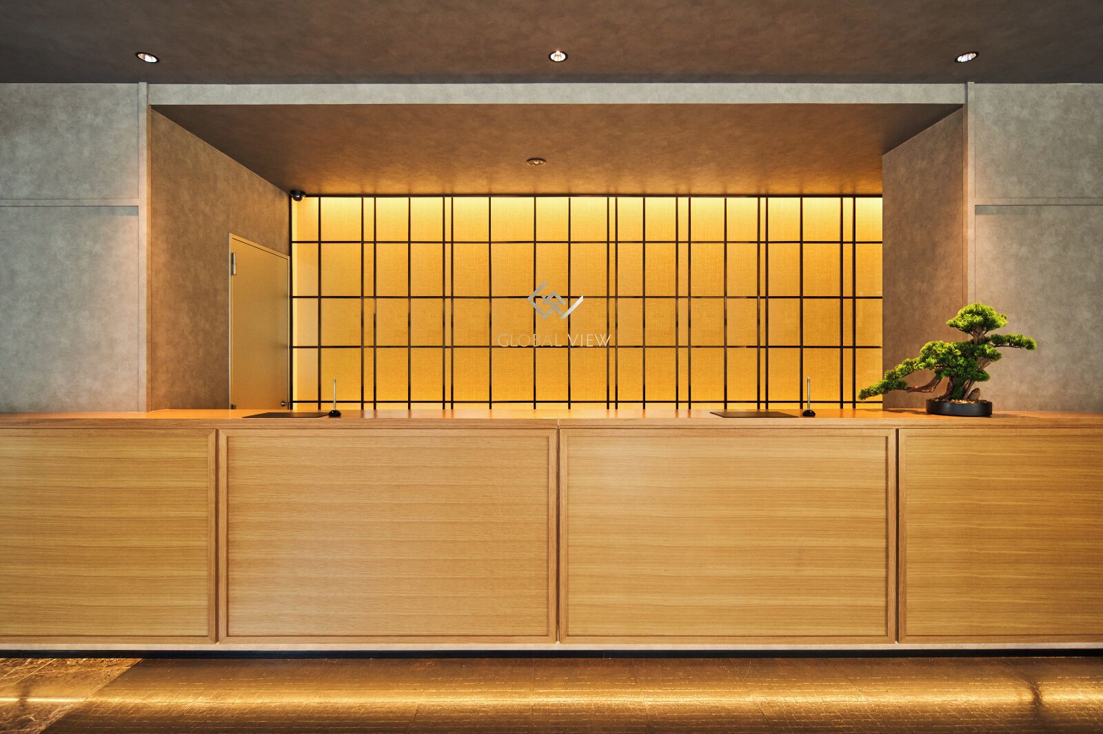 Un mostrador de recepción con un panel iluminado con diseño de cuadrícula, un logotipo y un bonsái.