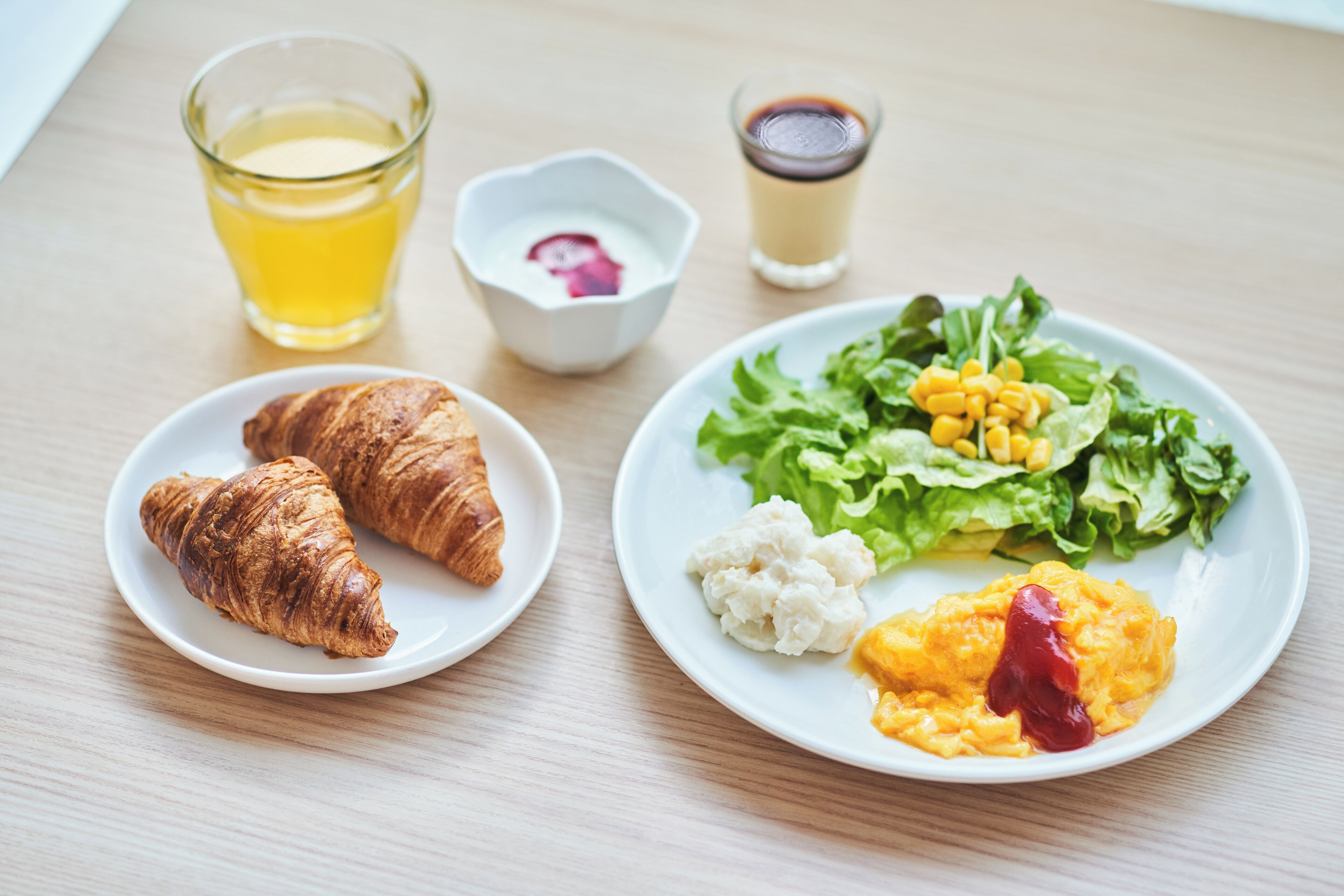 A plate with croissants, salad, and a glass of juice on a wooden table.