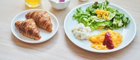 A plate with croissants, salad, and a glass of juice on a wooden table.